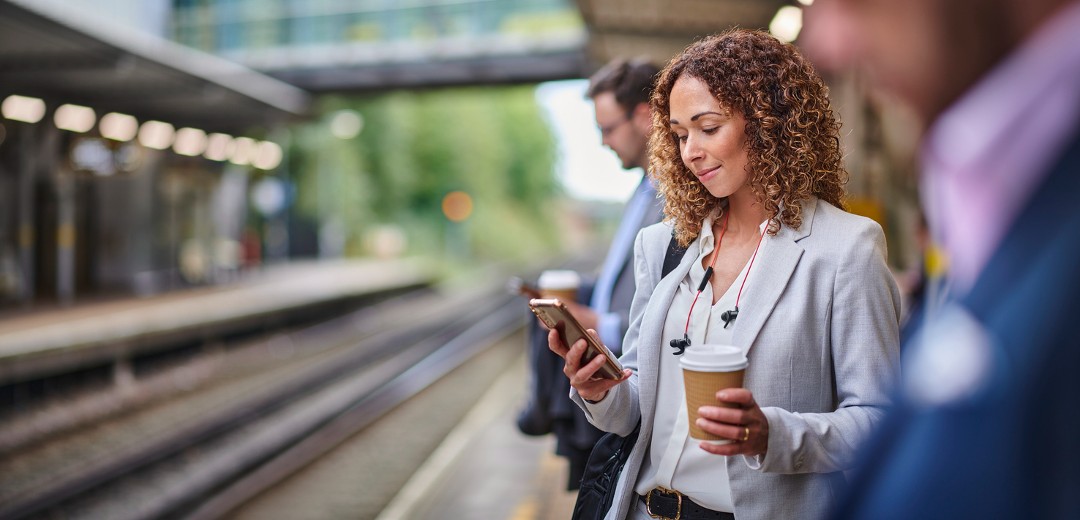 A women looking at phone with coffee in another hand on railway platform