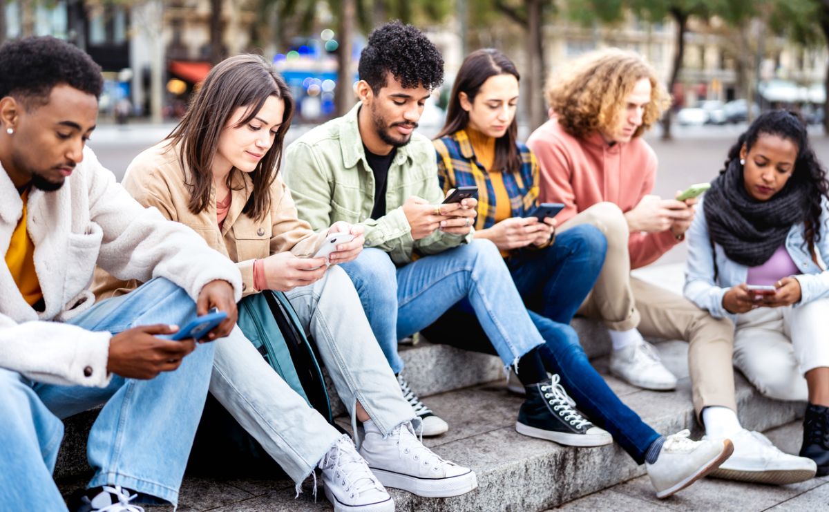 friends group using mobile smart phone sitting at university college yard