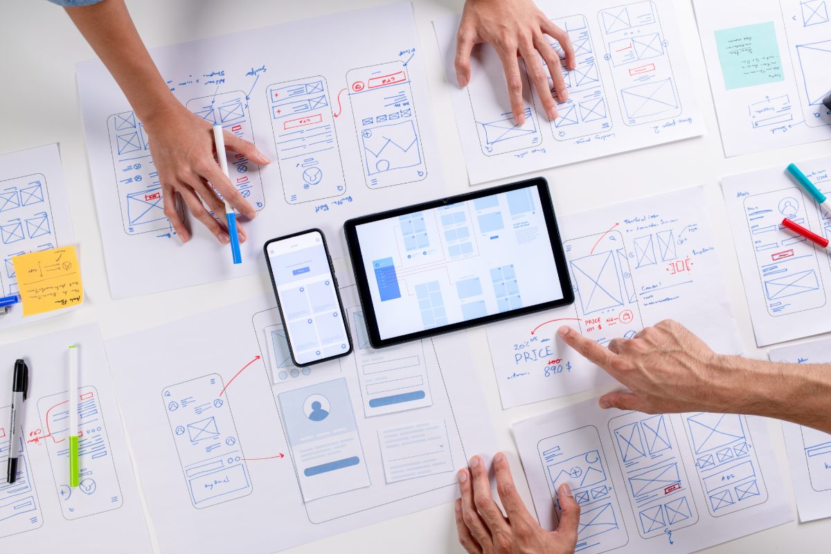 The 2026 Guide to Estate Agent Websites 4 UX/UI designers discussing and brainstorming on wireframes for a website and mobile app prototype